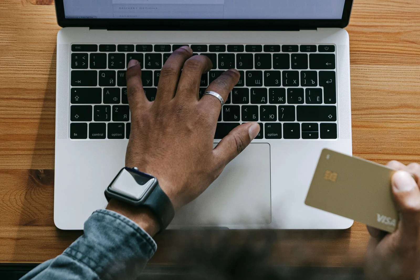 Van bovenaf gefotografeerde handen die op een laptop typen met een bankpas in de rechterhand